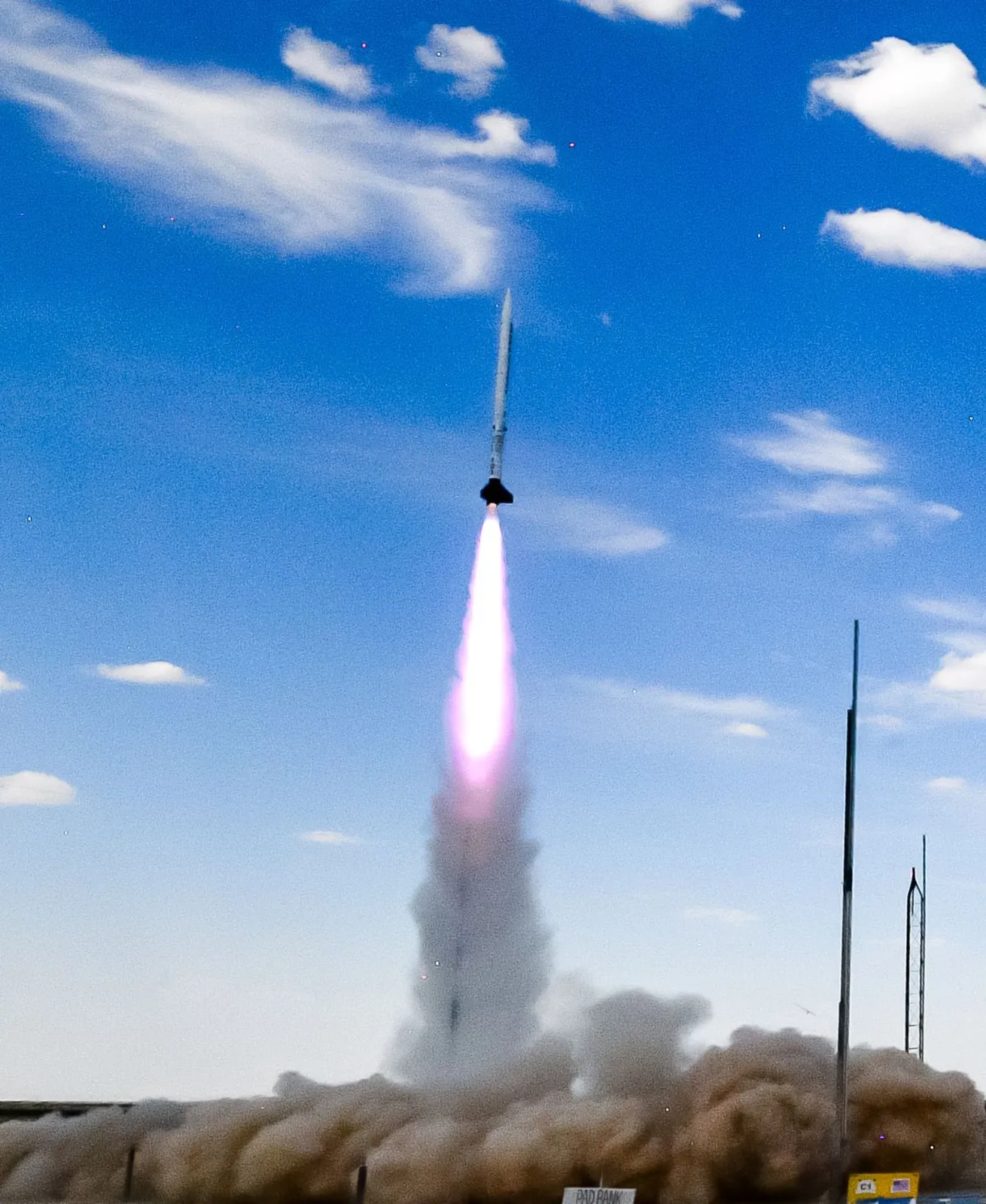 A rocket leaving the launch rail on a column of smoke under a blue sky