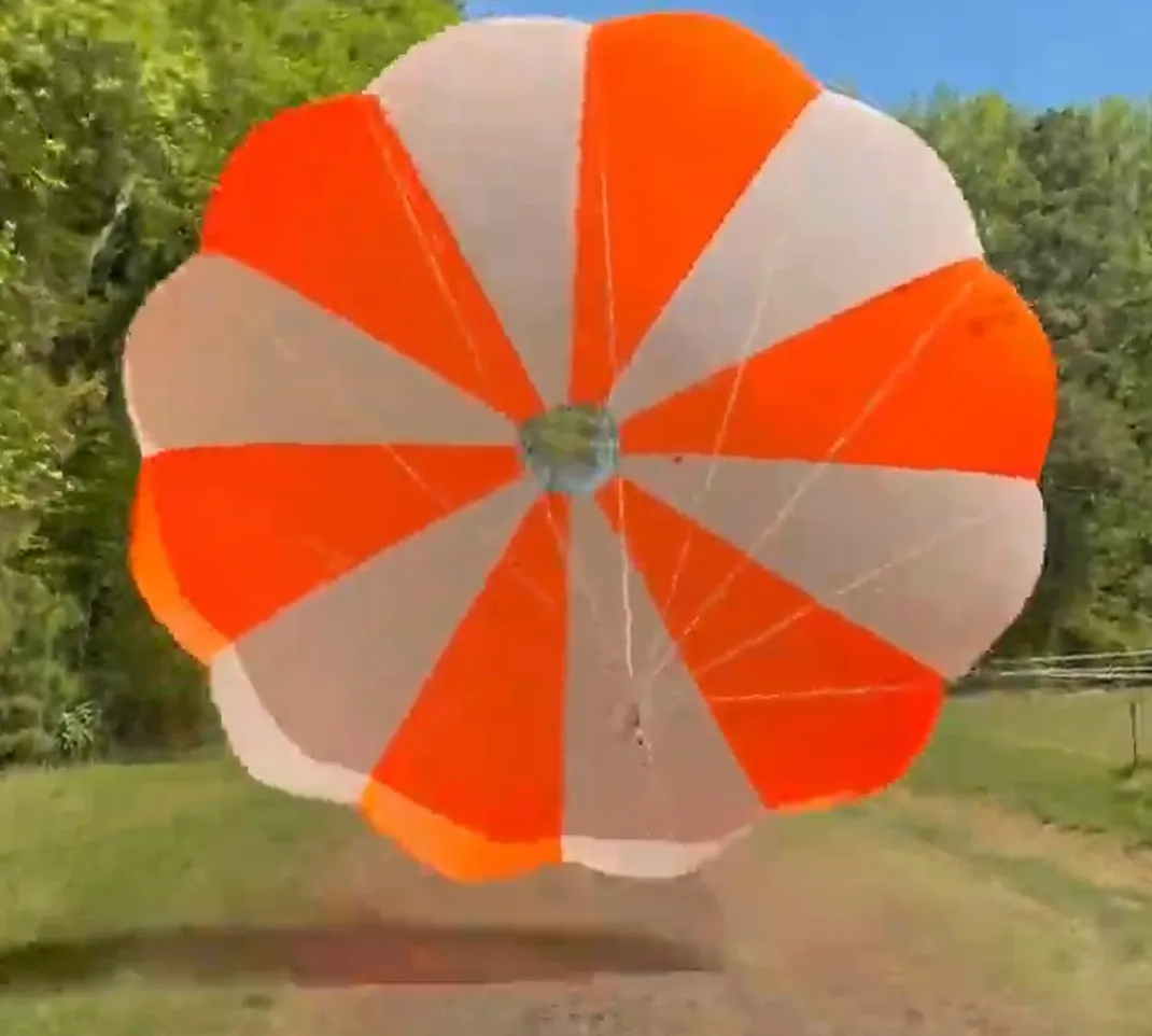 An orange and white parachute fully inflated near the ground