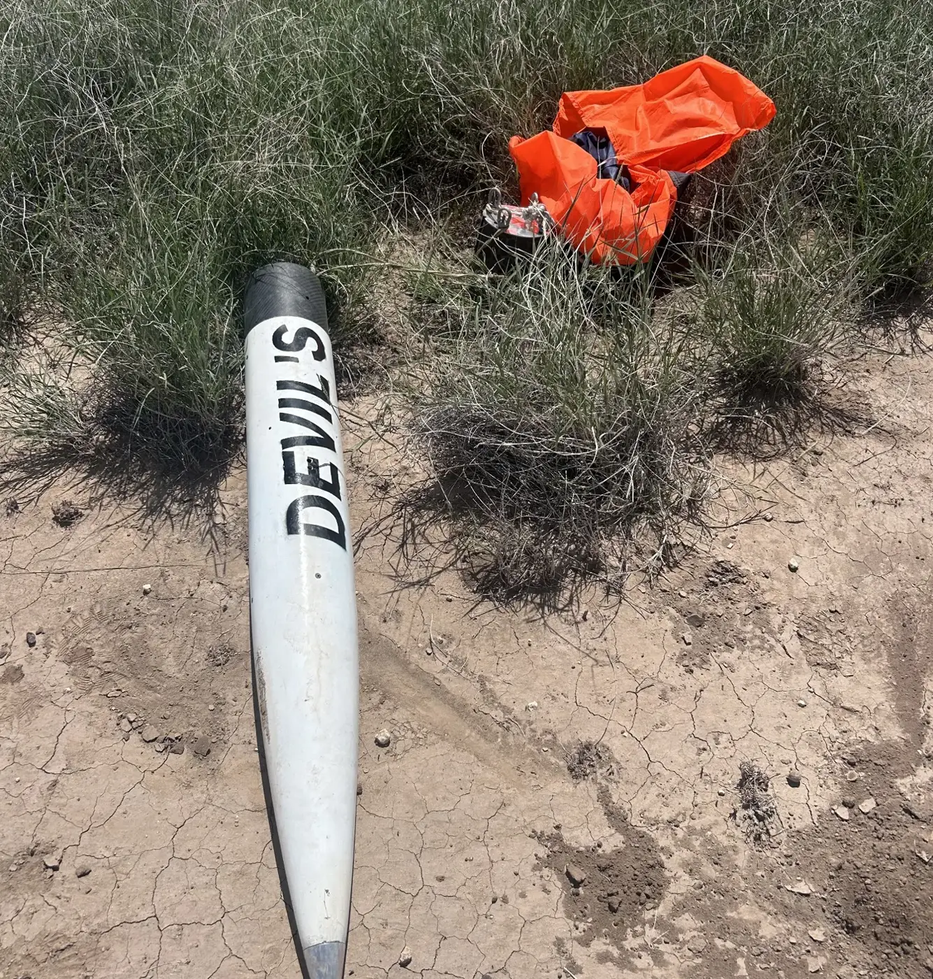 The recovered rocket body, labeled DEVIL'S, lying in grass with its orange parachute
