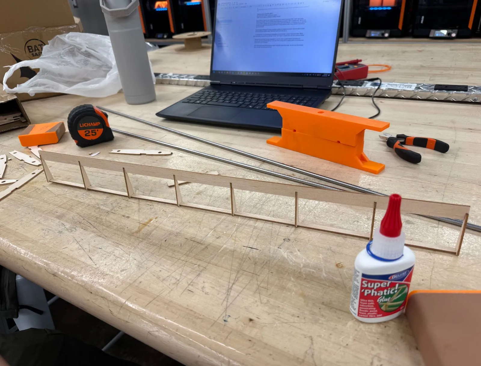 Wing ribs being assembled on a workbench next to a laptop and glue